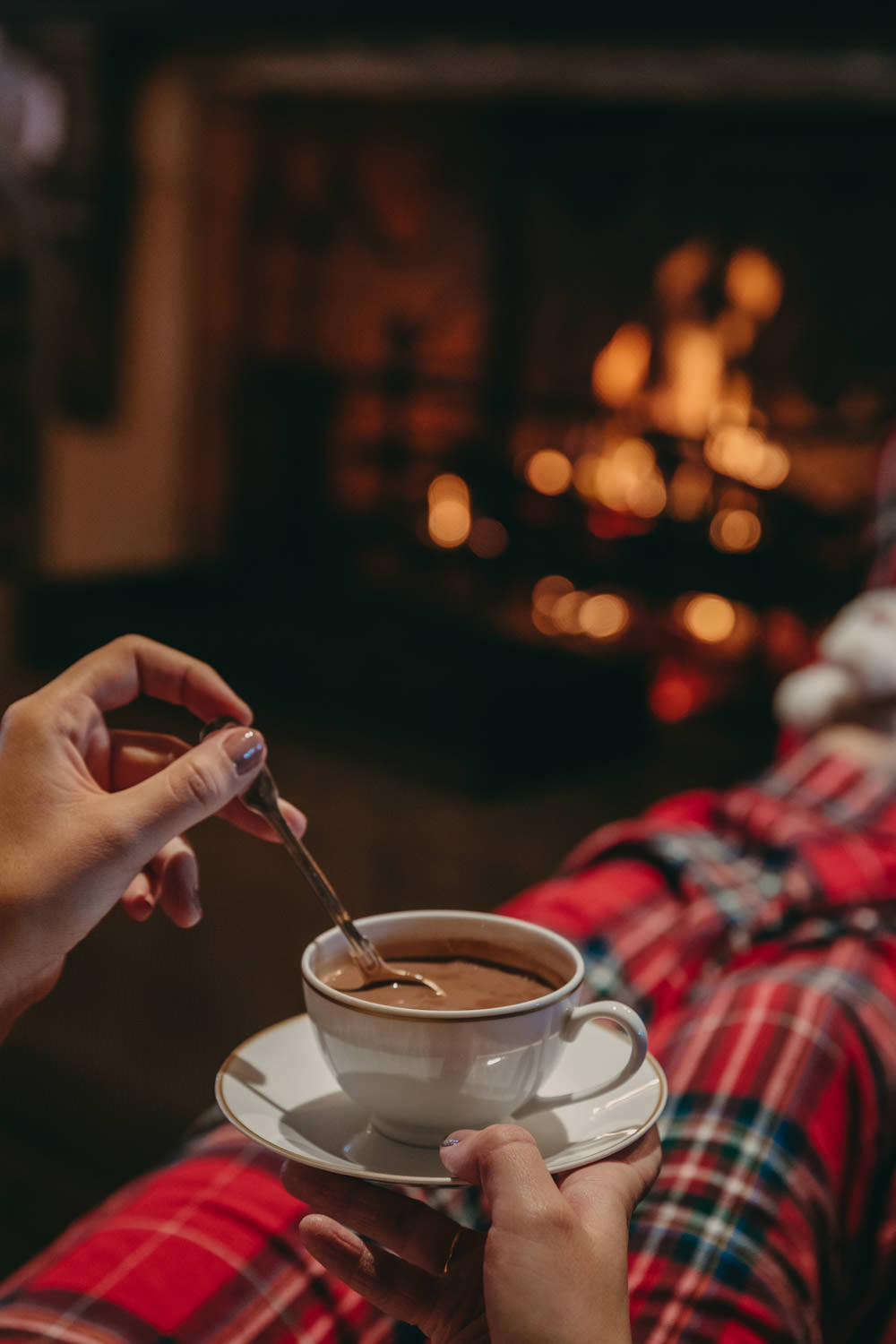 a girl's hand holding a cup of hot chocolate in plaid pajamas by the fireplace at airelles courchevel