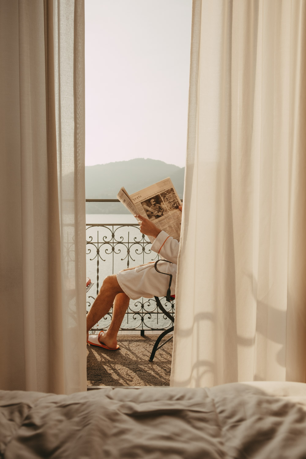 a man reading newspaper with views of lake como from grand hotel tremezzo