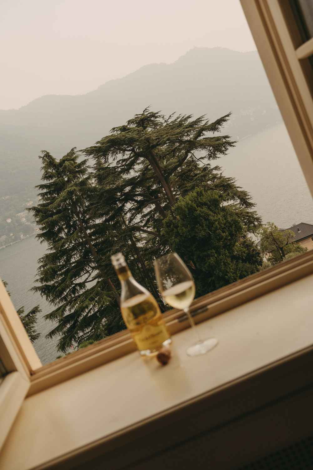 champagne bottle and a glass on the edge of a window overlooking lake como at passalacqua